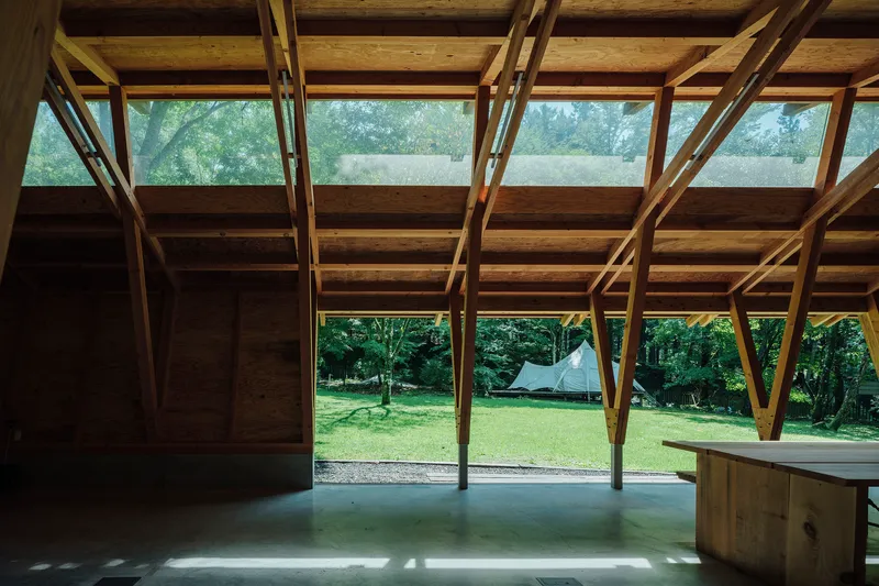 Open interior framing onto a grassed clearing with diagonal timber braces and a ribbon of high windows