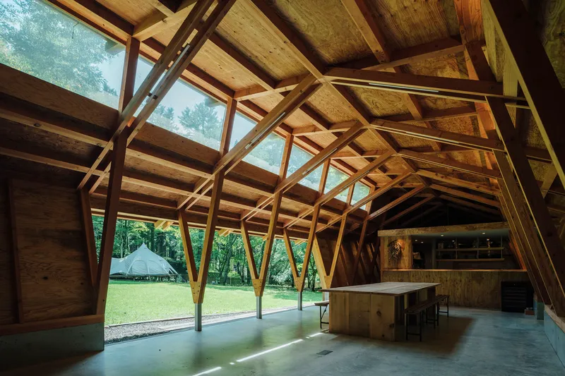 Interior space with exposed timber structure framing views to the green lawn and trees outside