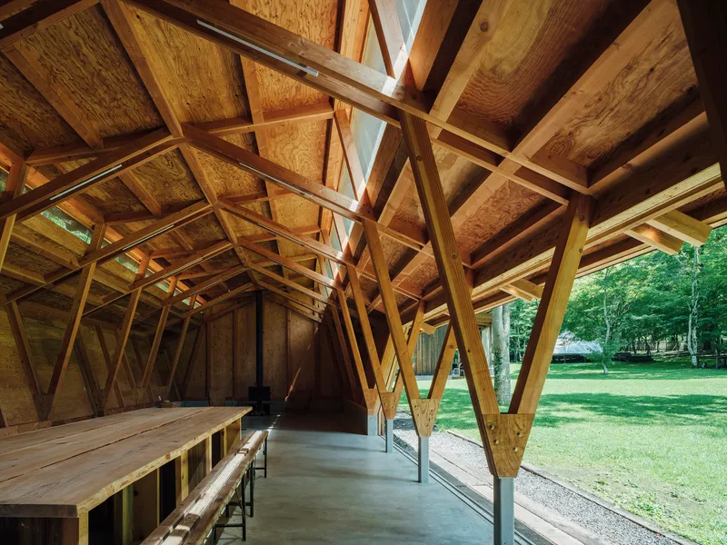 Interior corridor with diagonal timber columns and plywood-lined walls opening to the surrounding park
