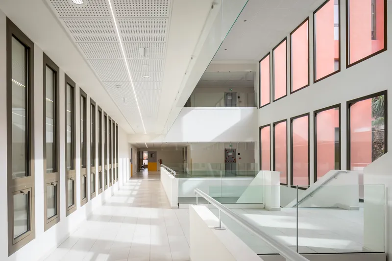 White tiled corridor with repetitive window frames and perforated ceiling panels under daylight