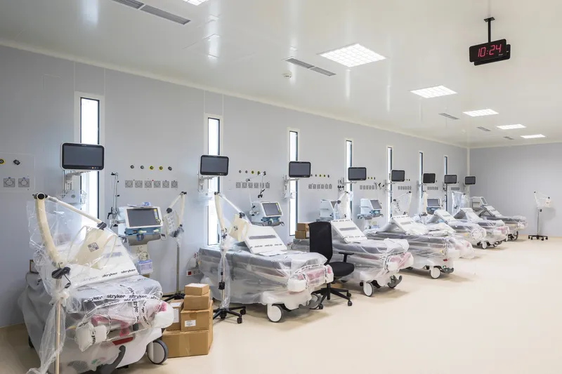 Row of dialysis stations with wrapped beds and overhead monitors beneath a digital clock
