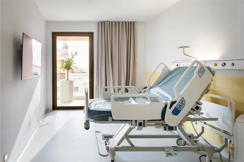 Patient room with adjustable bed, yellow headwall panel and glazed door to terrace
