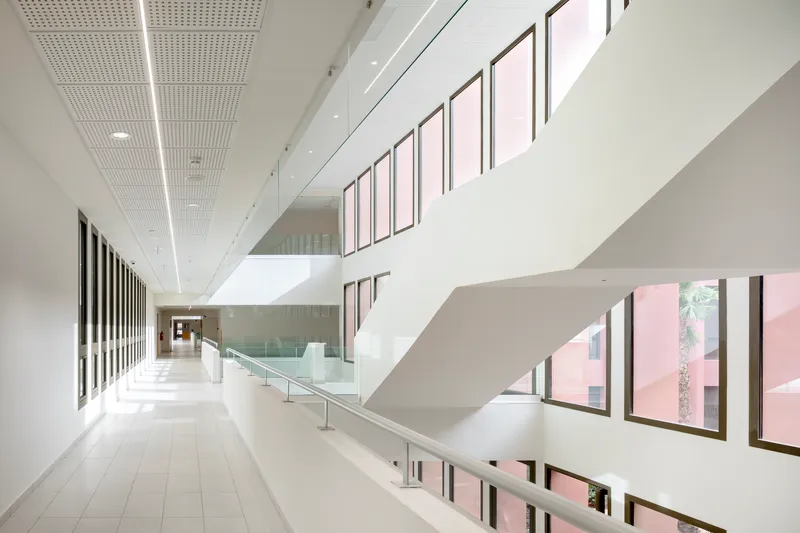 Multilevel circulation space with glass balustrades and pink courtyard views through vertical windows