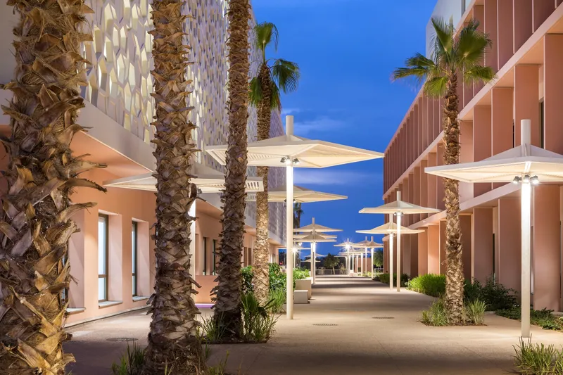 Pedestrian walkway lined with palm trees and white shade canopies at dusk