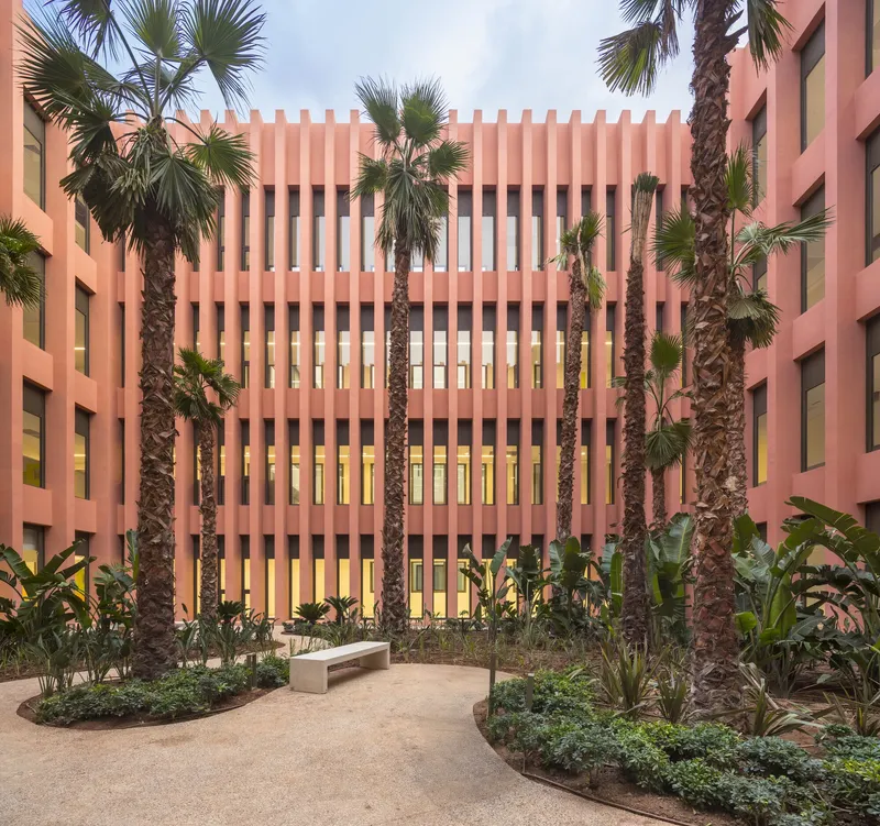 Courtyard view with palm trees framing the vertical terracotta brise-soleil screen and planted beds below