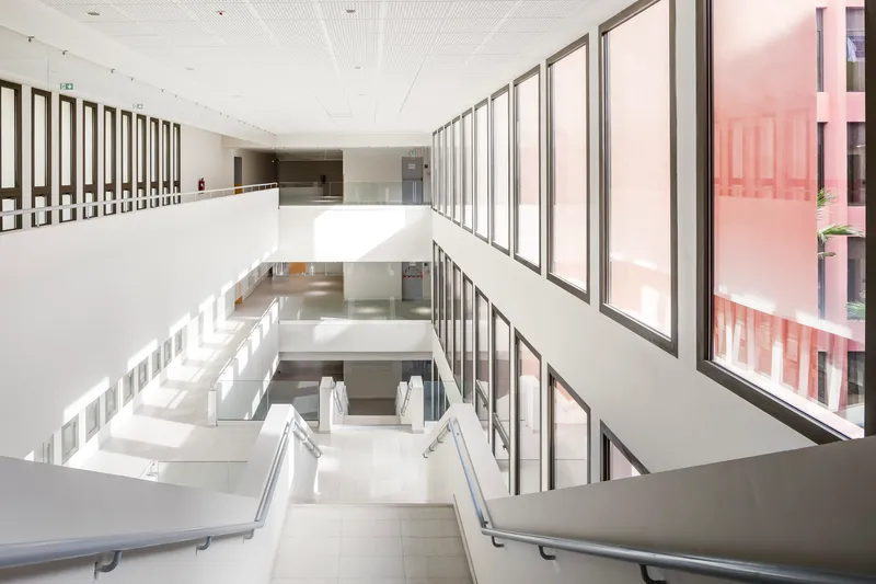 Interior atrium with white walls, continuous glazing overlooking a courtyard, and a staircase descending three levels