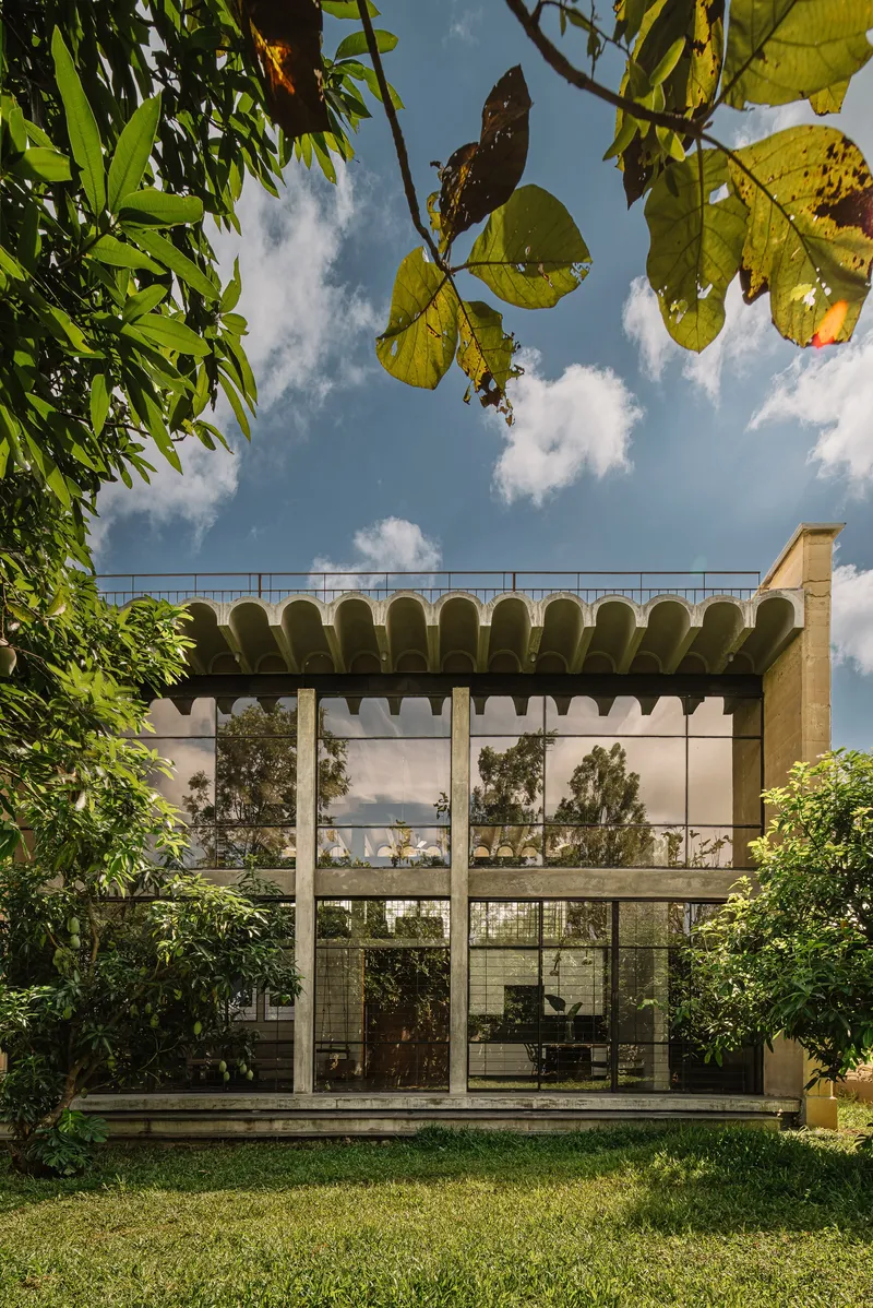 Two-story glass facade beneath scalloped canopy viewed through overhanging tree branches