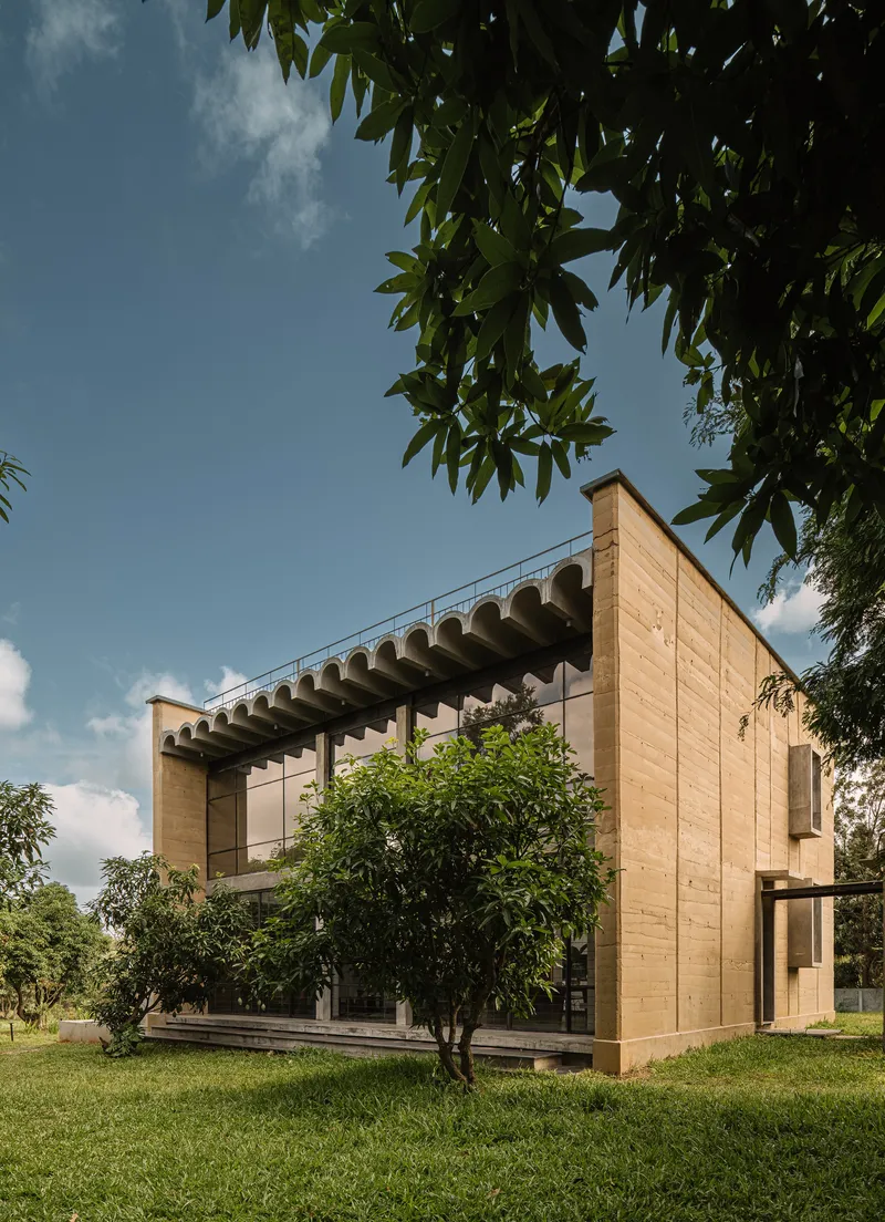 Corner elevation showing rammed earth walls and scalloped canopy amid scattered trees and lawn