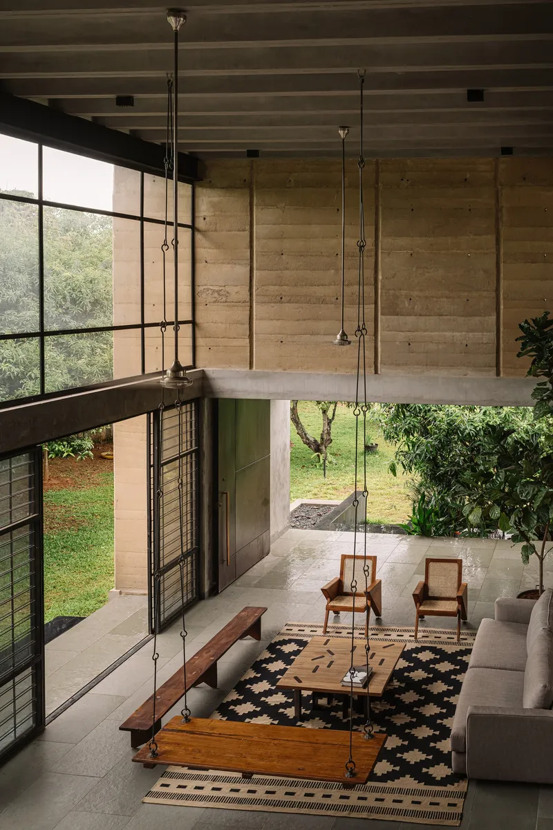 Double-height living room with exposed concrete ceiling joists and suspended swing seat overlooking the garden