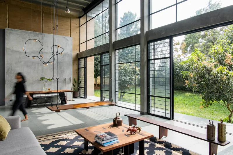 Living space with steel-framed doors opening to garden while a person walks past the concrete wall