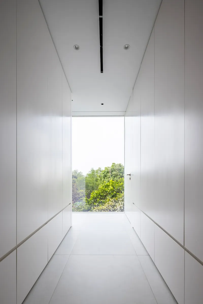 White corridor with full-height storage cabinetry terminating at a window framing treetops