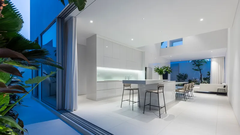 Open kitchen and dining area at dusk with bar stools and sliding glass doors framing tropical plants