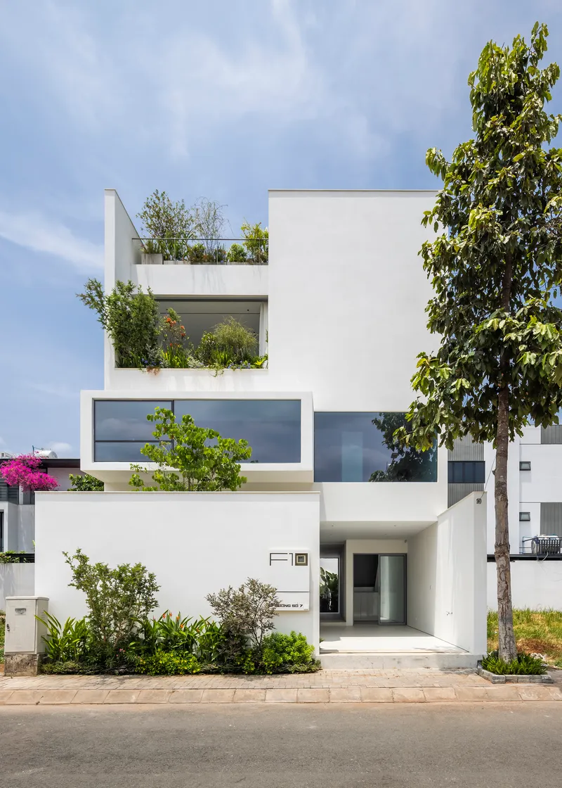 Street view of the white stucco facade with planted terraces and a street tree in afternoon light