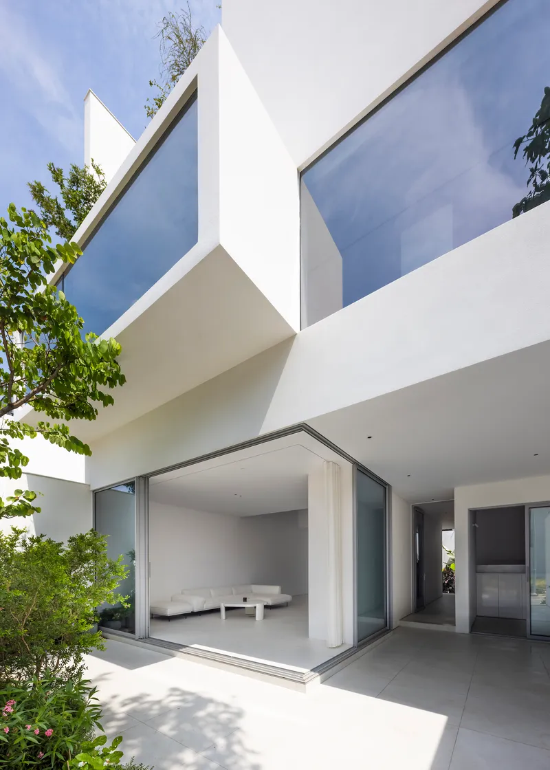 Ground floor terrace with sliding glass doors opening to the interior and trees framing the white volumes above