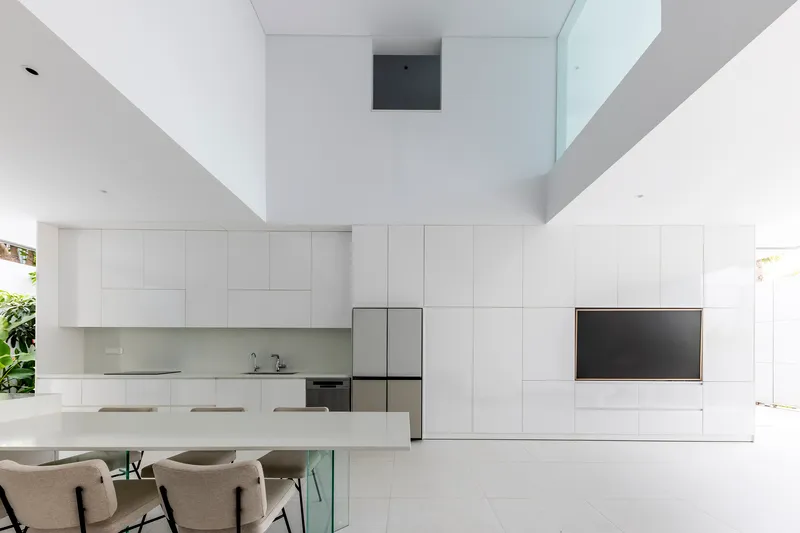 Double height void above the white kitchen and dining table with view to upper skylight