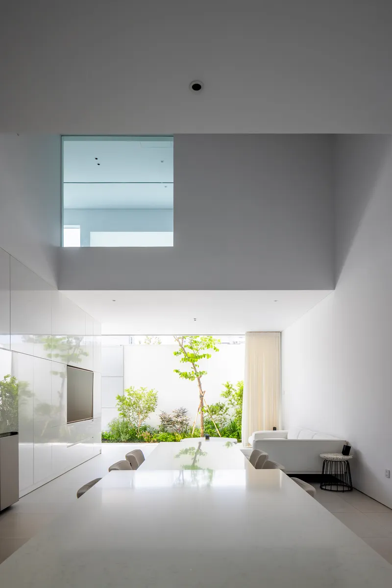 Dining area with mezzanine void overhead and planted courtyard visible through the glass wall