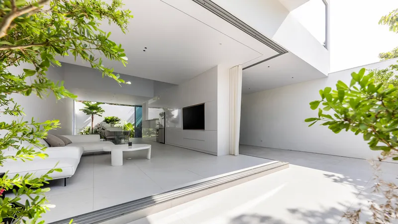 Open living space with sliding glass doors framed by tropical planting in dappled sunlight