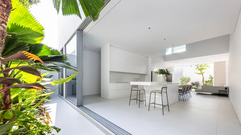 Kitchen island with bar stools opening to dining area and courtyard garden with palm fronds
