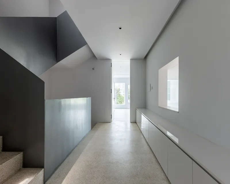 Upper level corridor with angled ceiling planes and terrazzo flooring leading to window