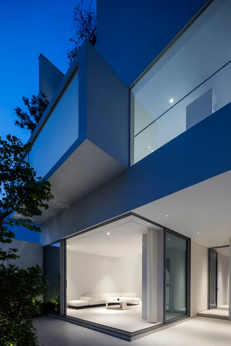 Stacked cantilevered volumes with floor-to-ceiling glass and white rendered walls at blue hour