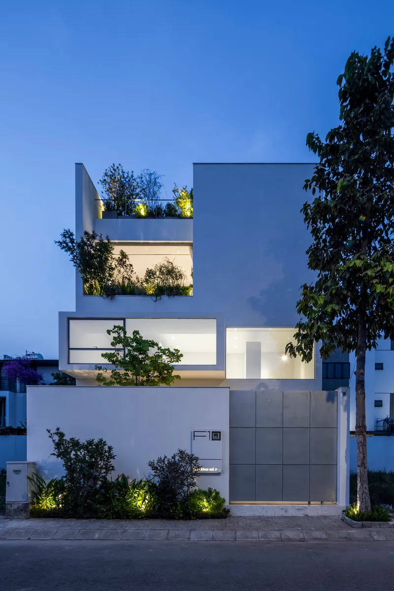 Street facade at dusk showing stacked volumes with planted terraces and uplighted vegetation