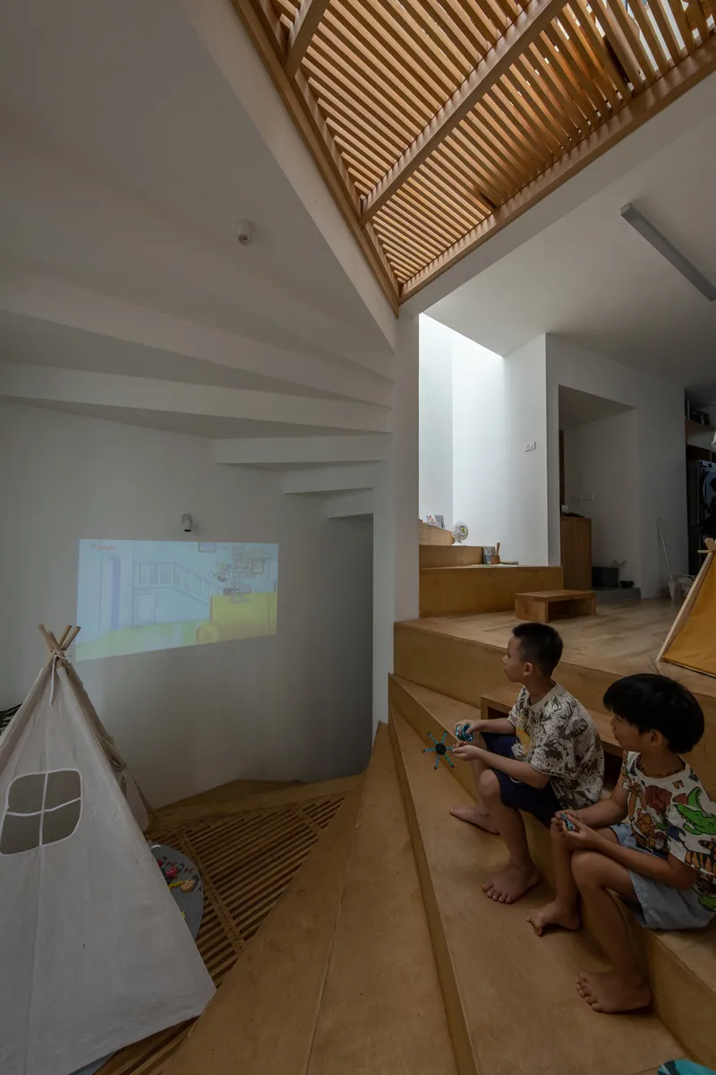 Double-height space with slatted timber ceiling and two children seated on the stepped platform
