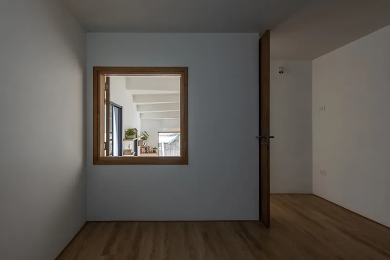 White room with timber-framed window opening onto an adjacent space with exposed ceiling beams