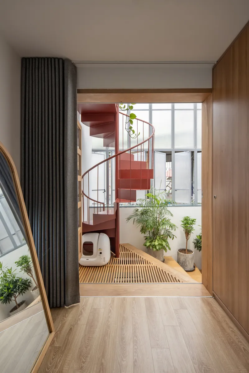 Red spiral staircase in glass-enclosed balcony space with potted plants and timber slat floor