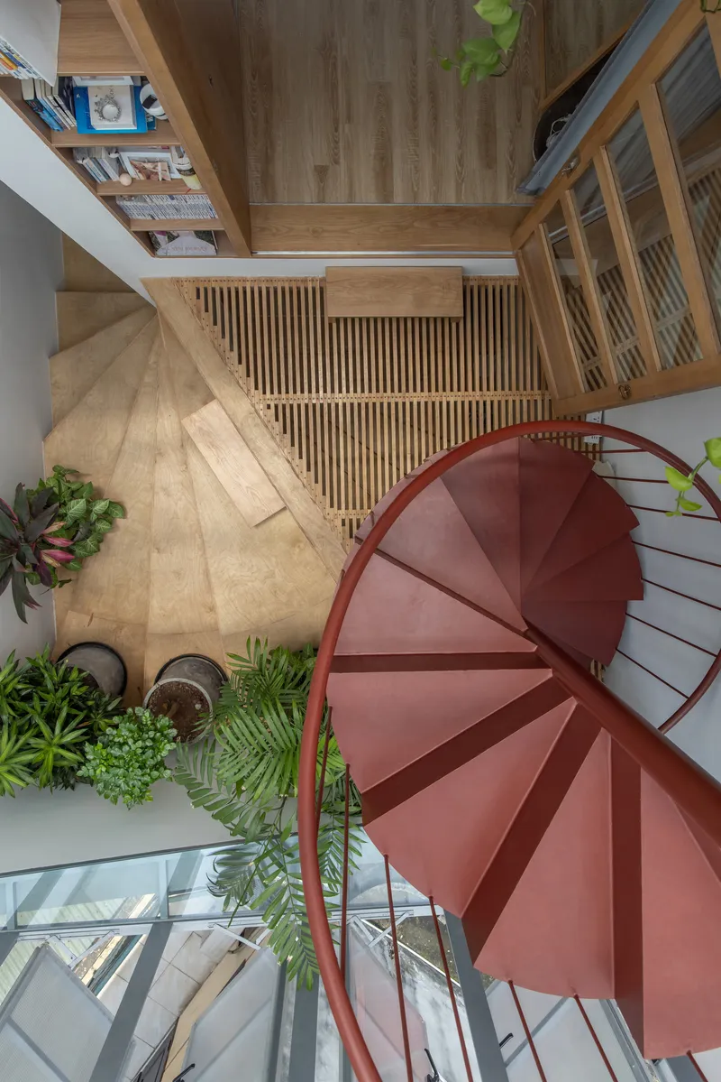 Top-down view of red spiral staircase surrounded by timber screens and potted greenery