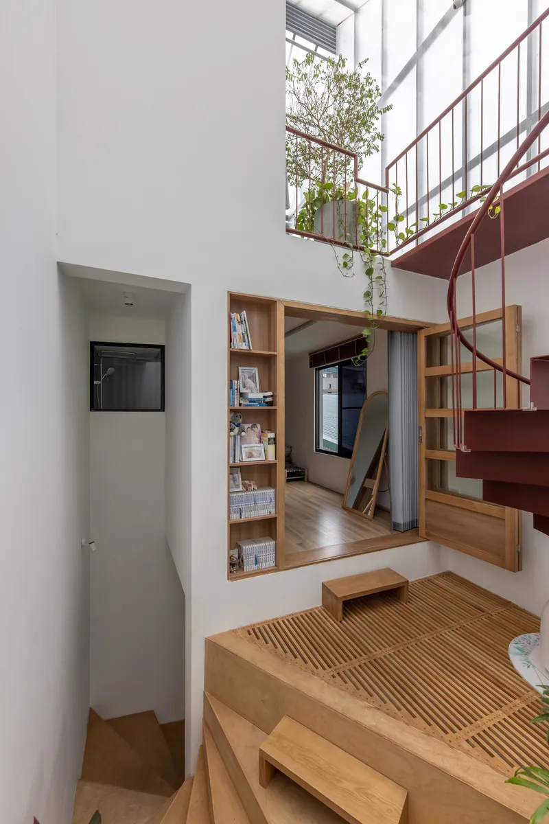 Double-height living space with timber staircase, built-in shelving, and mezzanine planting visible above