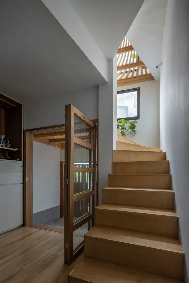 Timber staircase rising toward slatted ceiling with natural light filtering through and window at landing