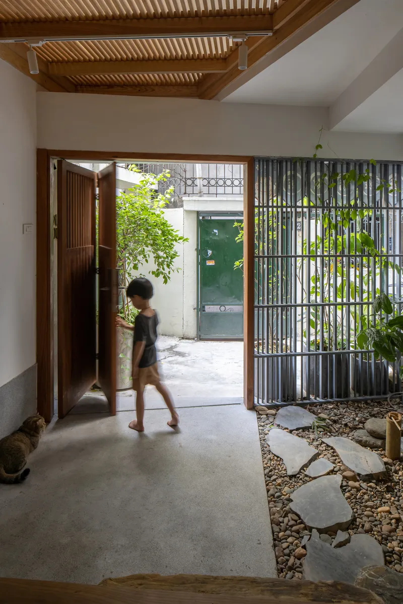 Entry vestibule with folding timber door opening to pebbled courtyard and person walking through in motion
