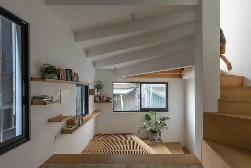 Interior reading nook with timber platform, slatted floor, floating shelves, and person ascending the staircase