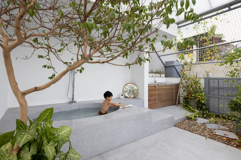 Rooftop terrace with concrete tub, small tree, and person bathing among planted beds