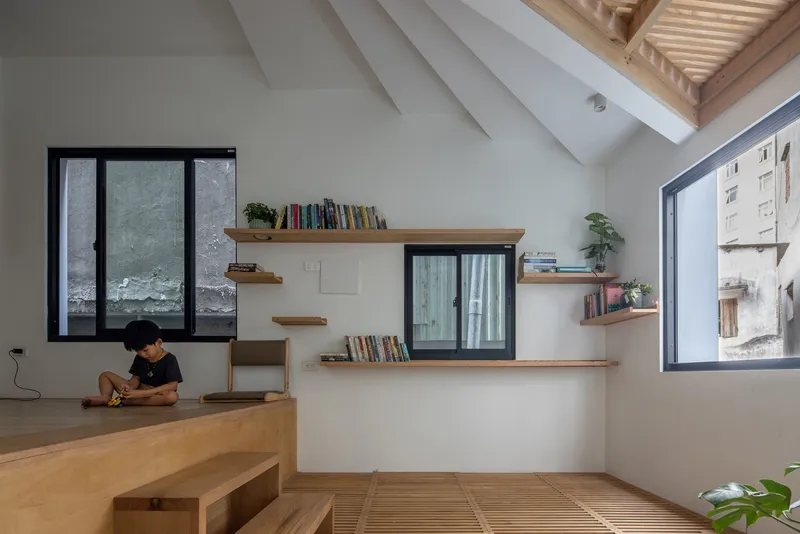 Living area with timber shelving, vaulted ceiling with exposed slats, and a person seated on the raised floor