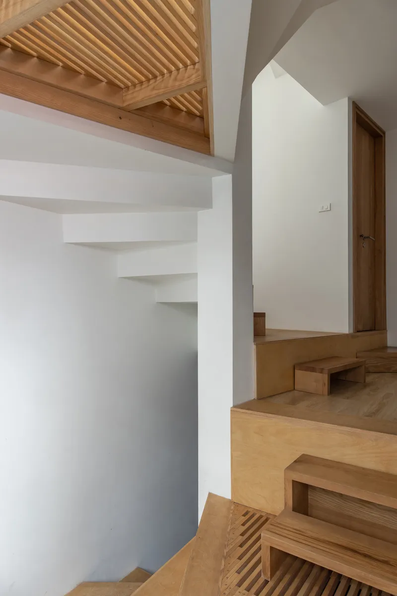 Timber staircase with integrated storage and corner shelving beneath a slatted wood ceiling skylight
