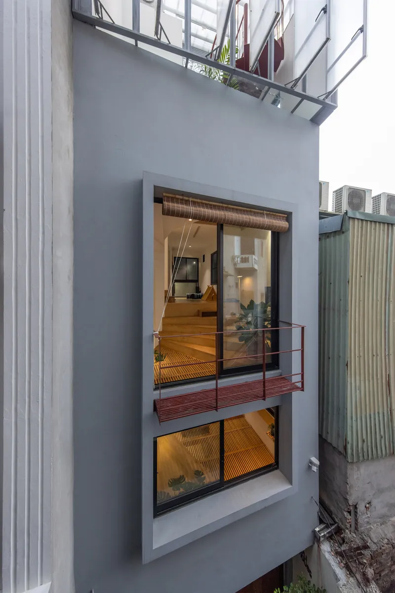 Exterior facade showing stacked glazed openings and a red metal balcony between neighbouring walls at dusk