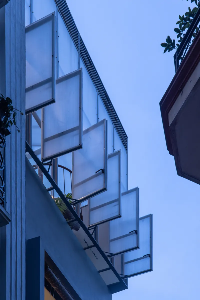 Translucent polycarbonate wall with metal stair and planters ascending the facade under a blue evening sky