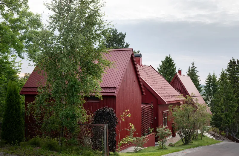 Red vertical siding and matching metal roofs framed by birch trees and evergreens under overcast skies