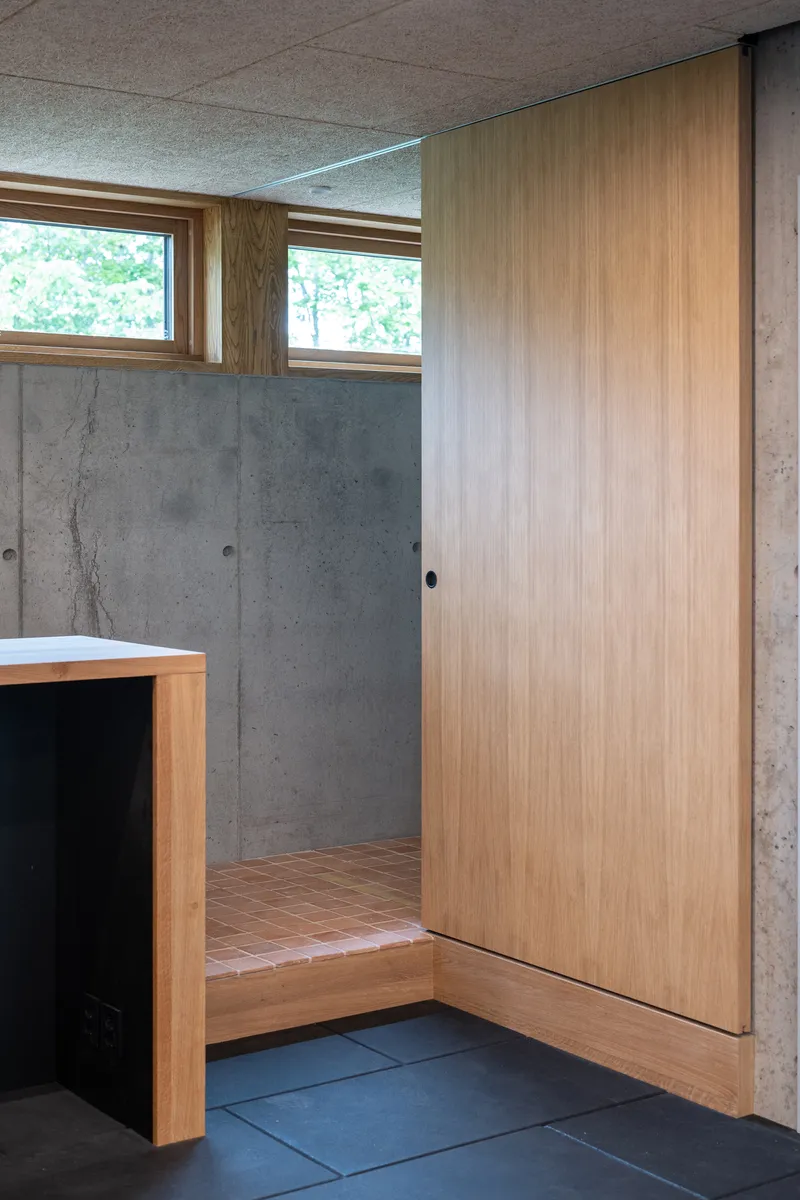 Interior corner with tall timber sliding door, poured concrete walls and clerestory windows overlooking greenery