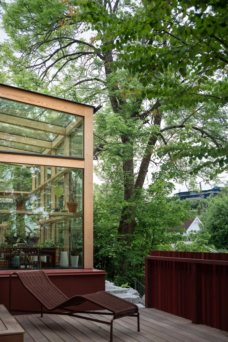Timber-framed glass extension beside a deck with lounge chair and red corrugated fence