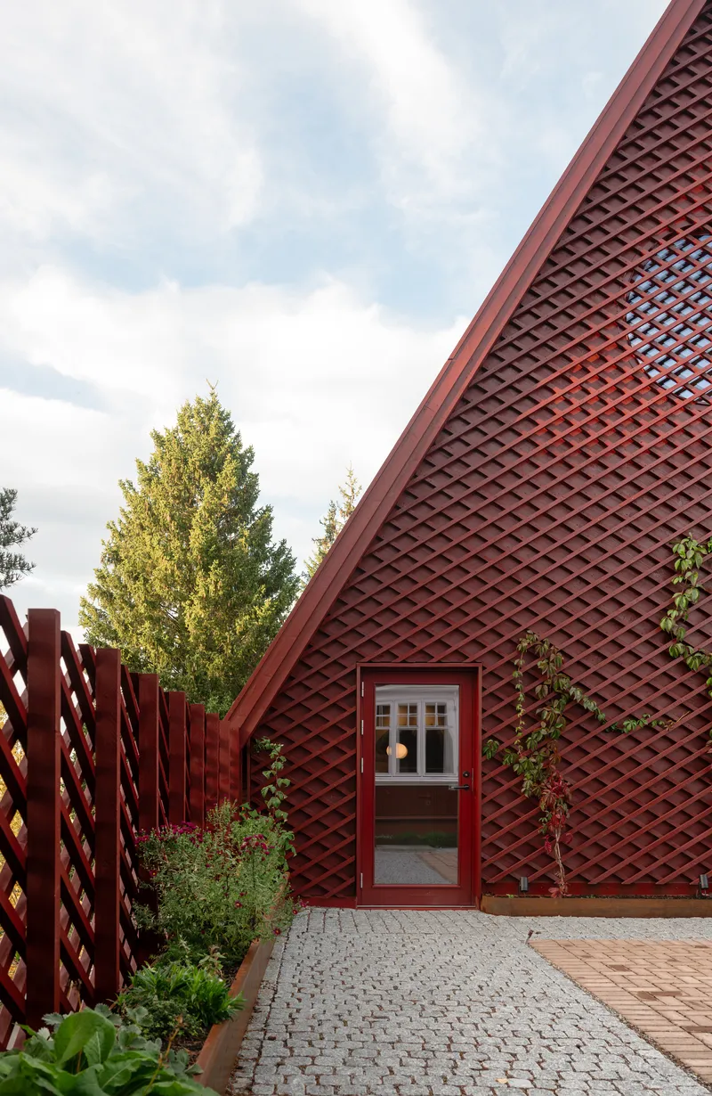 Red lattice fence and gable facade with diagonal trellis cladding under partly cloudy skies