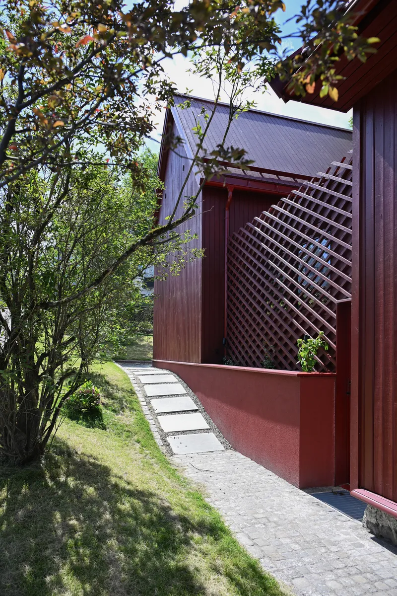 Red timber slatted screen and cladding along a stone paved pathway beneath leafy tree branches