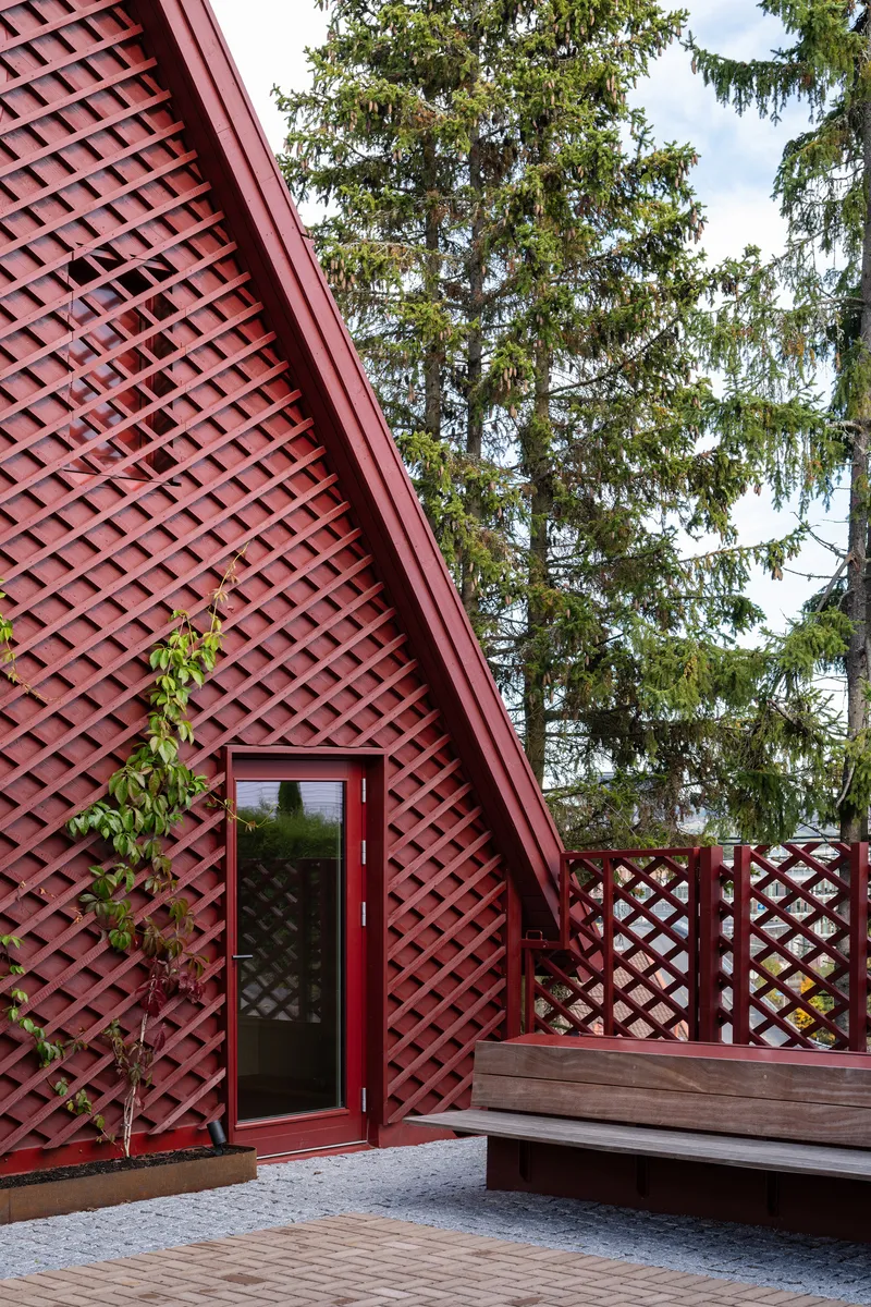 Latticed red facade with glass entry door beside timber deck and diagonal trellis screening