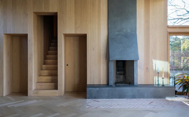Light timber interior with steel fireplace surround flanked by doorway and glimpse of staircase opening