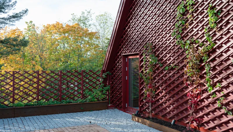 Red lattice screen wall with climbing vines beside a paved terrace under autumn trees