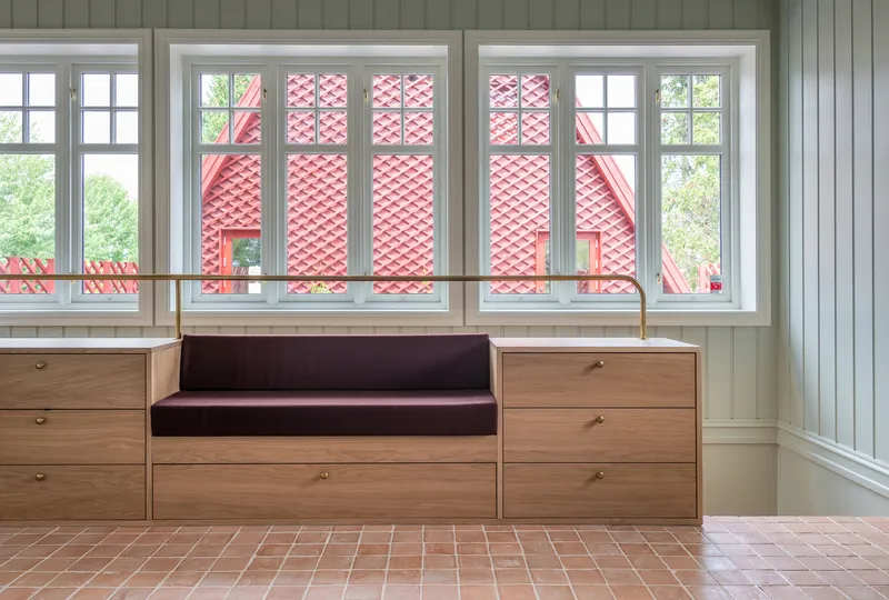 Built-in timber bench seat with drawers below white-framed windows overlooking red lattice facade