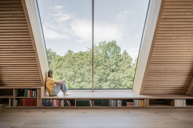 Person seated in a skylight window nook with timber slatted ceiling and built-in bookshelves