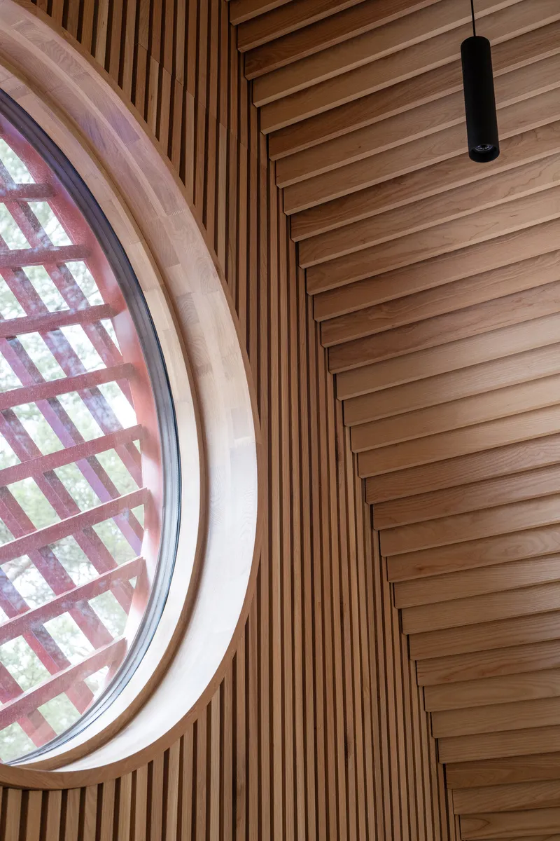 Circular window with gridded timber screen framed by vertical wood slats and horizontal ceiling battens