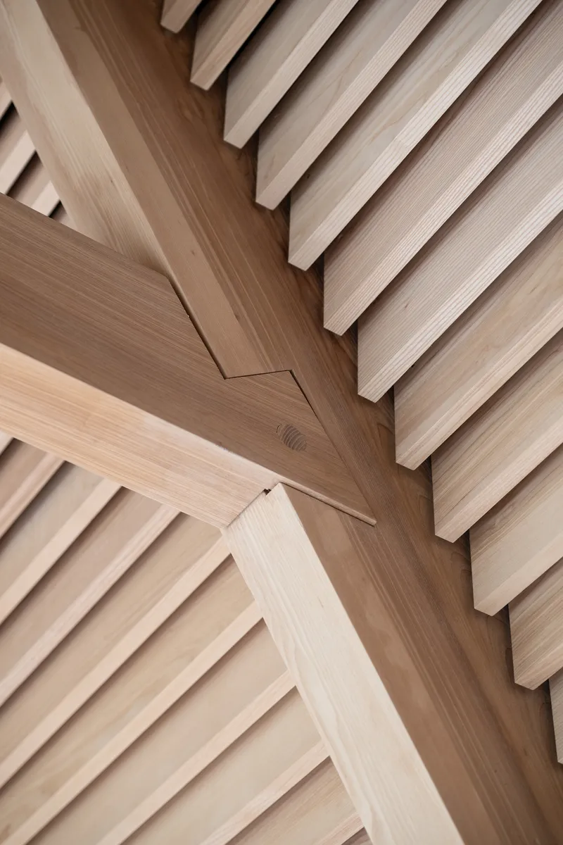 Detail of timber beam intersection with horizontal slatted ceiling panels meeting at an angle